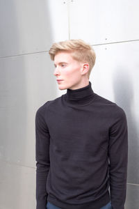 Portrait of young man looking away against wall