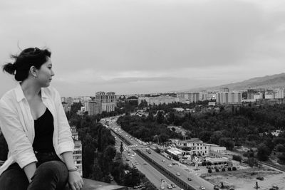 Young woman sitting on road in city against sky