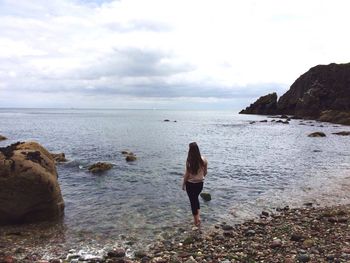 Rear view of woman standing on shore at beach against sky