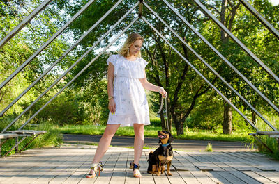 A beautiful blonde young woman with dog sitting next to her in the park.