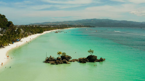 Topical white beach and willy's rock with tourists and hotels and sailing boat on boracay island. 