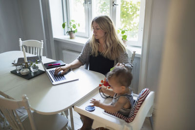 Mid adult woman using laptop while taking care of baby boy at home