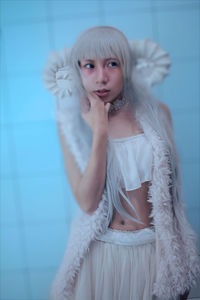 Portrait of young woman standing against white wall