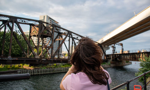 Rear view of woman looking at bridge over river against sky