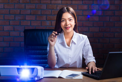 Smiling young woman using phone while standing against brick wall