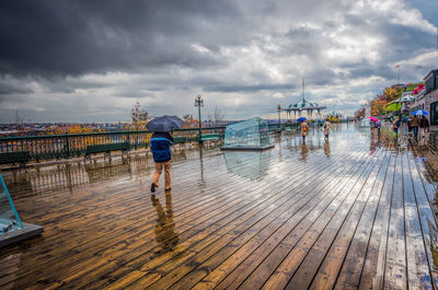 People walking on deck against cloudy sky during rainy season