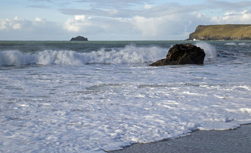 Waves splashing on rocks against sky