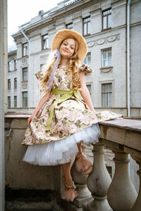 Little girl in dress and hat posing on the balcony