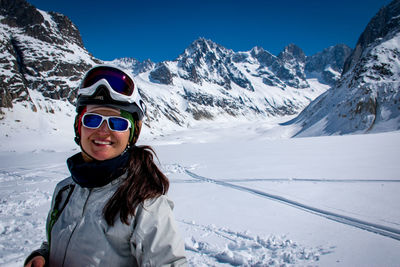 Portrait of smiling young woman on snowcapped mountain against sky