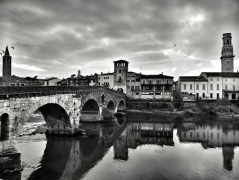 Arch bridge over river by buildings against sky in city