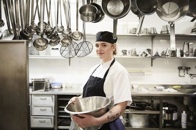 Portrait of confident female chef holding container in commercial kitchen