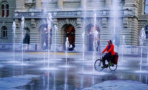 Rear view of man with bicycle on wet road during rainy season