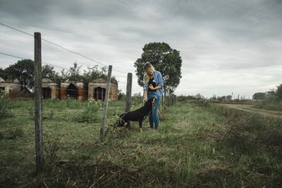 Woman with dog standing on grass against sky