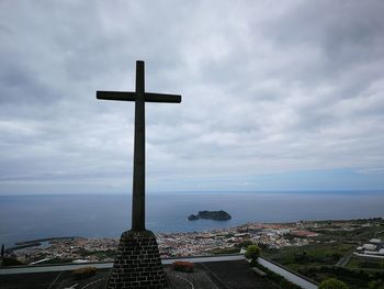 Cross by sea against sky in city
