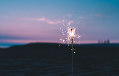 Firework display on land against sky at sunset
