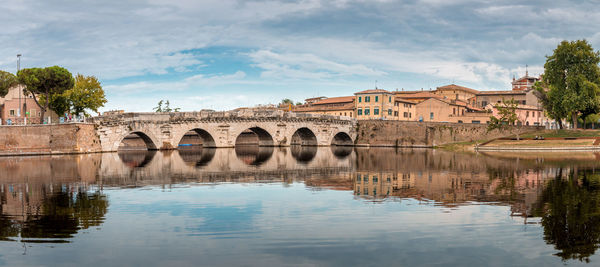 Arch bridge over river by buildings against sky