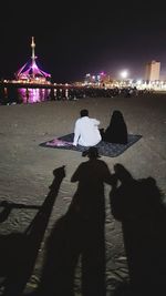 Rear view of couple sitting on illuminated city at night