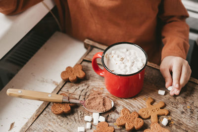 Children drink cocoa with marshmallows and christmas gingerbread man on a wooden background.