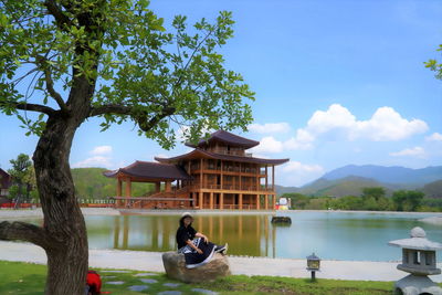 Woman sitting by lake against sky