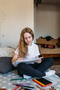 The girl after school plays at home, draws with pencils and felt-tip pens