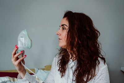 Woman wearing oxygen mask while sitting on bed against wall in hospital