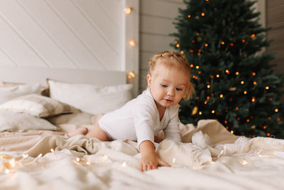 Happy cheerful baby little girl sitting smiling on a cozy bed at christmas holidays at home