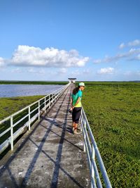 Woman on railing by sea against sky