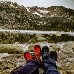 Low section of person on snowcapped mountain by lake