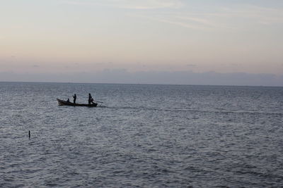 Silhouette people in sea against sky during sunset