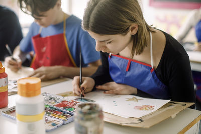 Female teenage student painting with brush during art class at high school