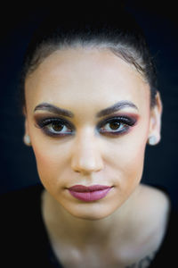 Close-up portrait of young woman against black background