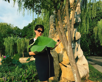 Portrait of woman wearing sunglasses while standing against trees