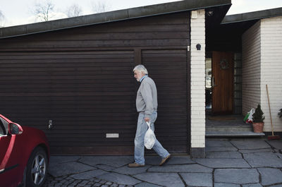 Side view of senior man carrying bag while walking by wall