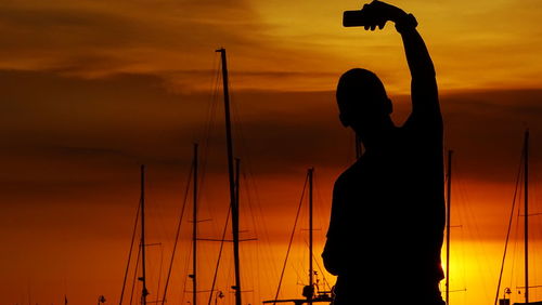 Silhouette person on sailboat against sky during sunset