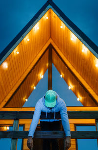 Man leaning over balcony by illuminated wooden cabin at night