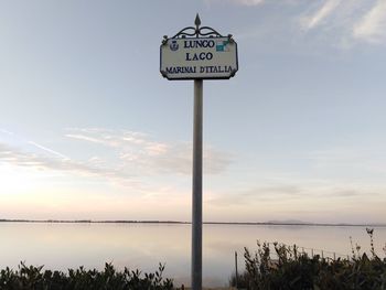 Information sign by sea against sky during sunset