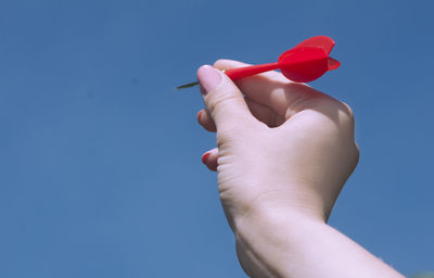 Cropped hand holding arrow against clear blue sky