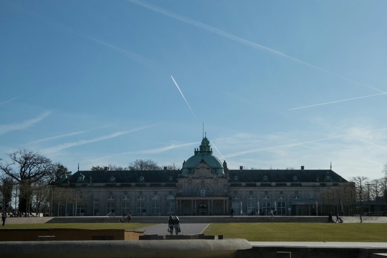 architecture, built structure, building exterior, sky, tree, men, lifestyles, person, blue, leisure activity, walking, incidental people, city, grass, sunlight, unrecognizable person, travel destinations, cloud - sky, tourist