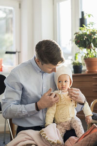 Father tying hood of baby girl at home