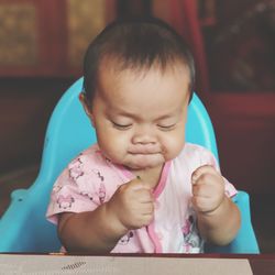 Close-up of cute baby girl making face while sitting on high chair at home