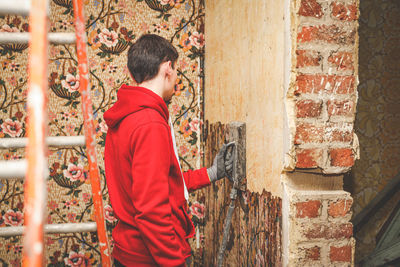 A young caucasian guy removes retro wallpaper using a steamer machine in an old abandoned house.