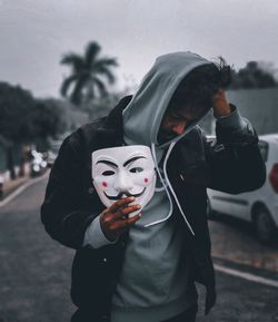 Portrait of man wearing mask standing on street against sky