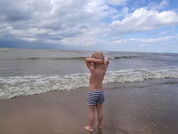 Full length of shirtless boy standing on beach against sky