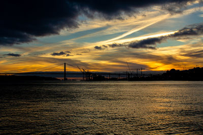 Silhouette bridge over sea against sky during sunset