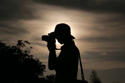 Side view of silhouette young man photographing against sky during sunset