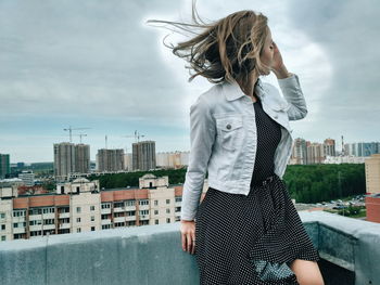 Young woman standing by cityscape against sky