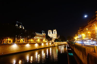 Illuminated buildings by river against sky at night