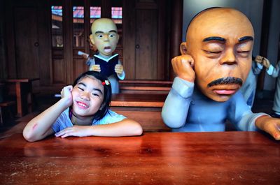 Portrait of cute smiling girl sitting by statue at table