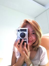 Portrait of smiling mid adult woman photographing with camera at home