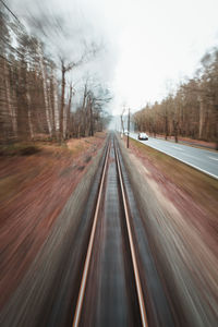 Blurred motion of road amidst trees in forest against sky